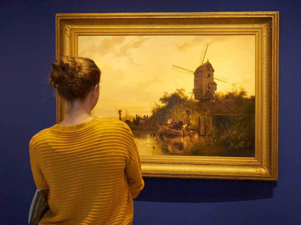 vrouw kijkt naar schilderij Waterland met molen van Wijnand Nuijen